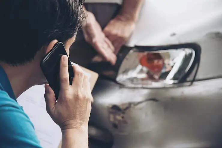 A person speaks on a mobile phone while inspecting car damage
